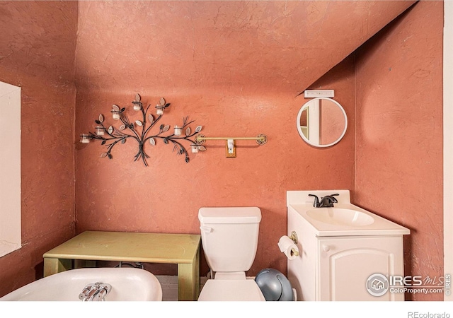 bathroom with toilet, a textured wall, vanity, and a bathtub