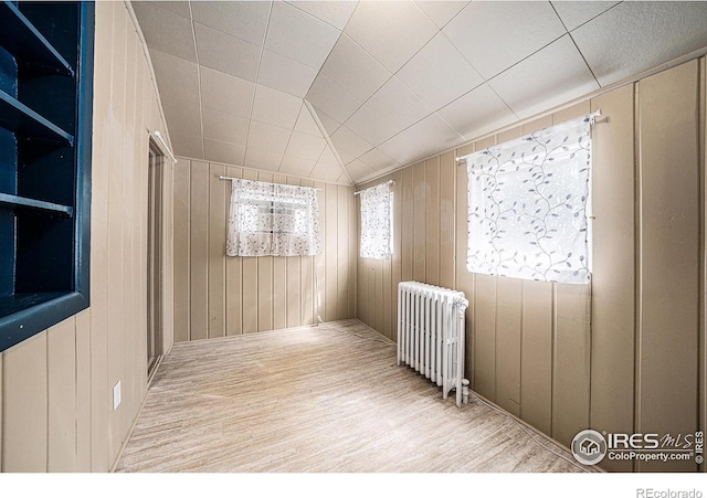 spare room with radiator heating unit, wood finished floors, and wooden walls