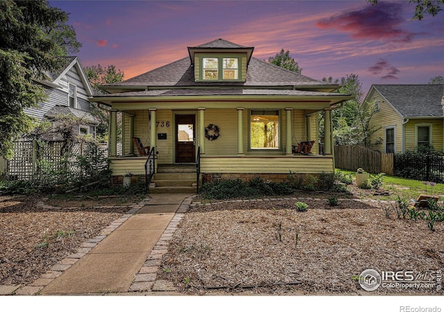 bungalow-style home featuring fence, covered porch, and roof with shingles