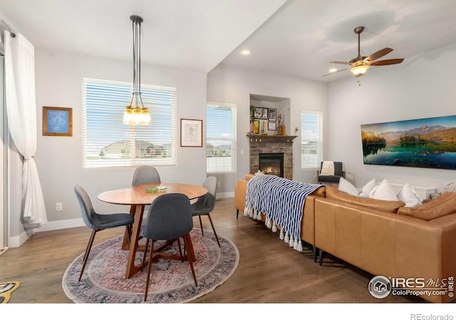 dining room with wood finished floors, a ceiling fan, recessed lighting, a stone fireplace, and baseboards