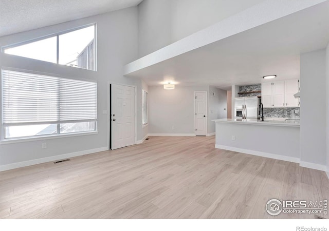 12525 E Tennessee Cir Unit E, Aurora, CO 80012 - unfurnished living room featuring light wood-style flooring, healthy amount of natural light, baseboards, and a towering ceiling