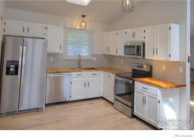 kitchen with appliances with stainless steel finishes, a sink, wooden counters, white cabinets, and vaulted ceiling
