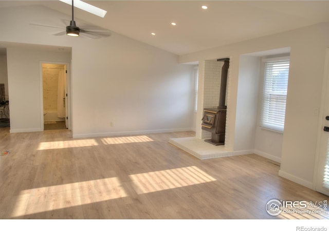unfurnished bedroom featuring light wood-type flooring, lofted ceiling, recessed lighting, a wood stove, and baseboards