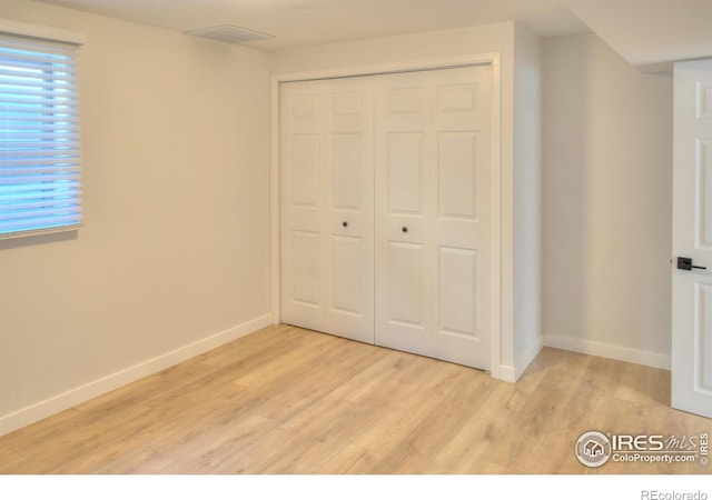 unfurnished bedroom featuring light wood-type flooring, a closet, and baseboards