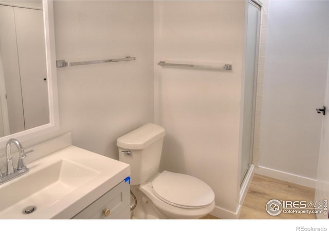 bathroom with wood finished floors, baseboards, toilet, a shower with shower door, and vanity