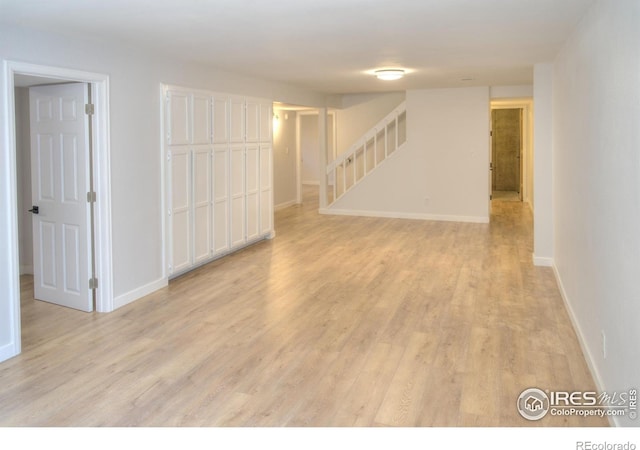 unfurnished room featuring stairs, light wood-style floors, and baseboards