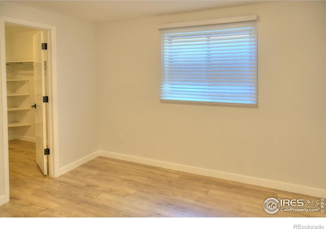 unfurnished bedroom with light wood-type flooring, a spacious closet, baseboards, and a closet