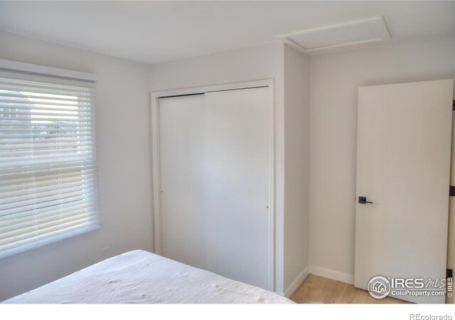 bedroom featuring attic access, light wood finished floors, a closet, and baseboards