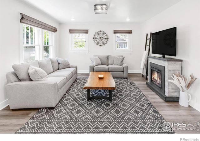 living room featuring wood finished floors, a glass covered fireplace, baseboards, and recessed lighting