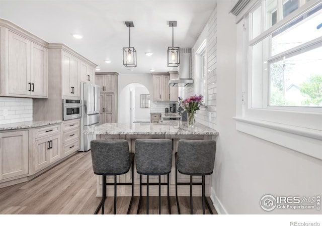 kitchen with wall chimney exhaust hood, stainless steel appliances, arched walkways, a breakfast bar, and recessed lighting