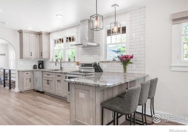 kitchen featuring wall chimney exhaust hood, appliances with stainless steel finishes, a sink, a kitchen breakfast bar, and decorative backsplash