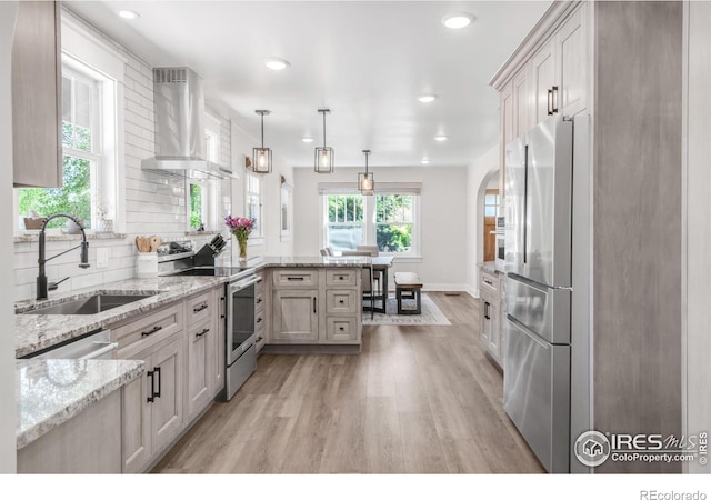 kitchen featuring stainless steel appliances, exhaust hood, a sink, a peninsula, and light wood finished floors