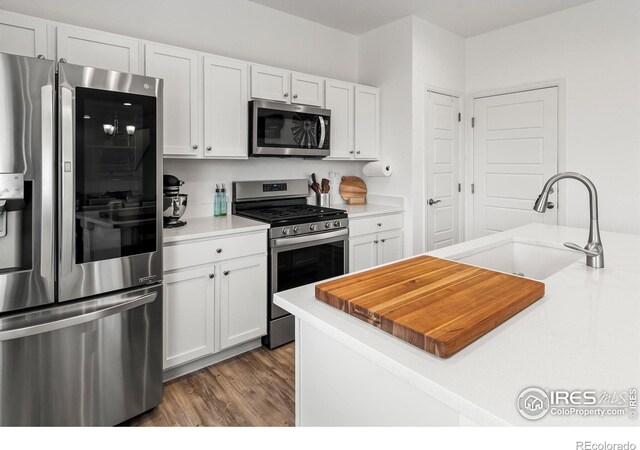 kitchen featuring appliances with stainless steel finishes, a sink, wood finished floors, white cabinetry, and light countertops