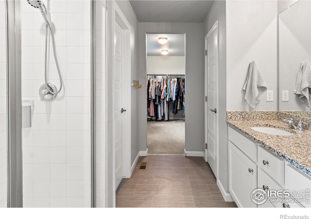 full bath featuring a stall shower, a spacious closet, vanity, and baseboards