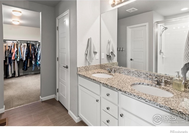 bathroom with baseboards, double vanity, a shower with shower door, wood finished floors, and a walk in closet