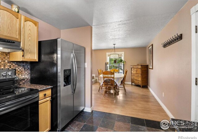 719 Marshall Pl, Berthoud, CO 80513 - kitchen with black range with electric stovetop, under cabinet range hood, stainless steel fridge, tasteful backsplash, and dark countertops