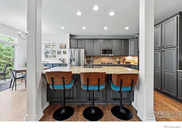 kitchen featuring stainless steel appliances, a sink, light wood-type flooring, light stone counters, and a spacious island