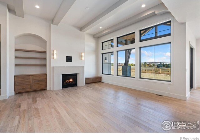 951 Warbling Dr, Windsor, CO 80550 - unfurnished living room featuring a lit fireplace, light wood-style flooring, recessed lighting, baseboards, and built in shelves
