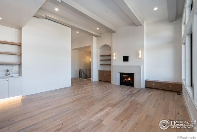 951 Warbling Dr, Windsor, CO 80550 - unfurnished living room with light wood finished floors, recessed lighting, beamed ceiling, a warm lit fireplace, and built in features