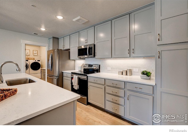 kitchen with washer and clothes dryer, stainless steel appliances, a sink, gray cabinetry, and decorative backsplash