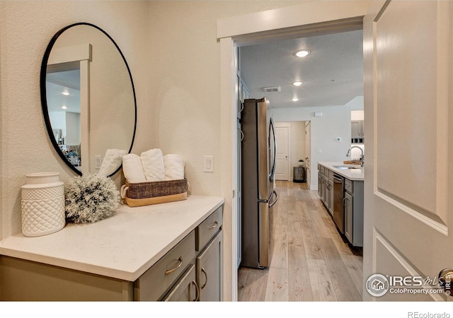 kitchen with a sink, appliances with stainless steel finishes, light wood finished floors, light countertops, and gray cabinets