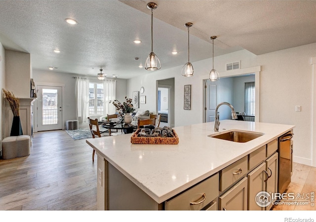 kitchen featuring a sink, a textured ceiling, open floor plan, light wood finished floors, and an island with sink