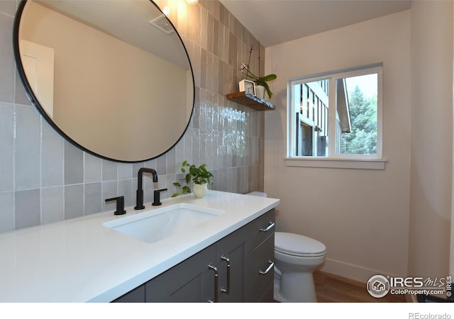 bathroom featuring tasteful backsplash, vanity, wood finished floors, baseboards, and toilet