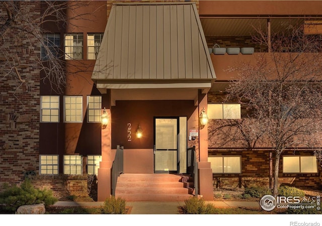 view of front of house featuring a standing seam roof, brick siding, stucco siding, and metal roof