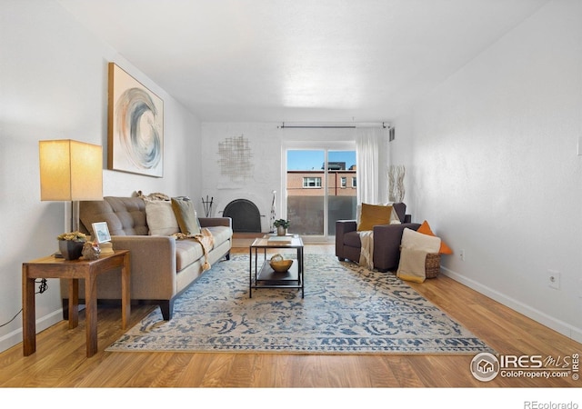 living room featuring wood finished floors, baseboards, and a large fireplace
