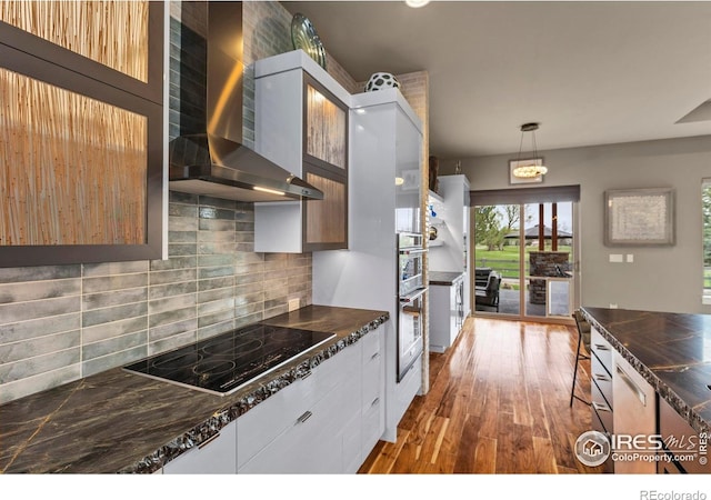 660 Deer Meadow Dr, Loveland, CO 80537 - kitchen featuring wall chimney range hood, black electric cooktop, dark countertops, wood finished floors, and decorative backsplash