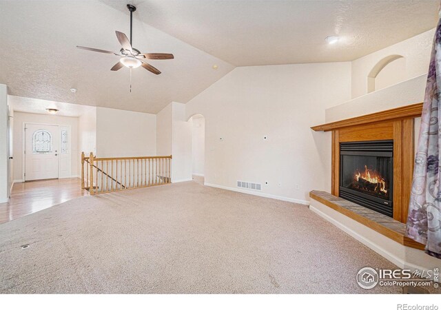 unfurnished living room with lofted ceiling, carpet flooring, baseboards, a glass covered fireplace, and a ceiling fan