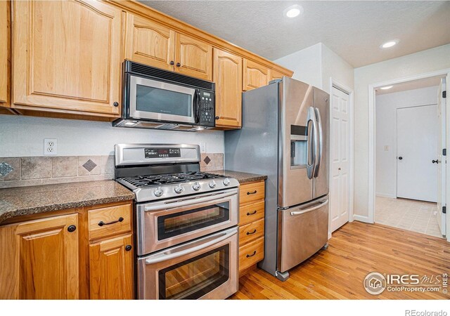 kitchen featuring appliances with stainless steel finishes, dark countertops, light wood finished floors, and recessed lighting