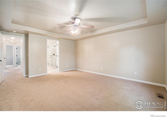 spare room with a tray ceiling, a ceiling fan, carpet, baseboards, and a textured ceiling