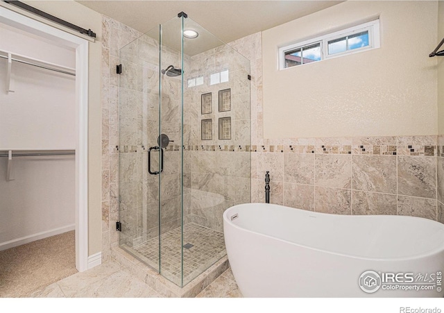 full bathroom with a stall shower, a freestanding tub, a spacious closet, and tile walls