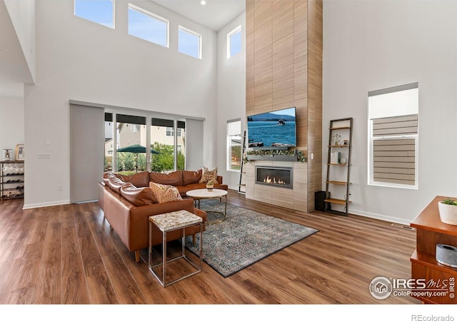 living room featuring a high ceiling, wood finished floors, a tiled fireplace, and baseboards