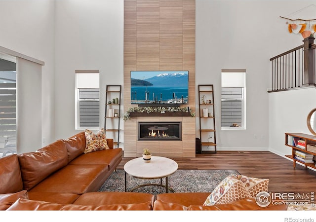 living area featuring a towering ceiling, wood finished floors, a tile fireplace, and baseboards