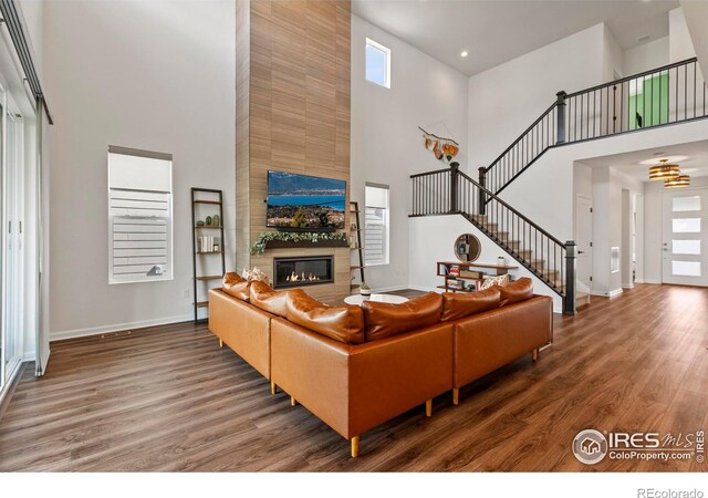 living room with a high ceiling, baseboards, wood finished floors, a large fireplace, and stairs
