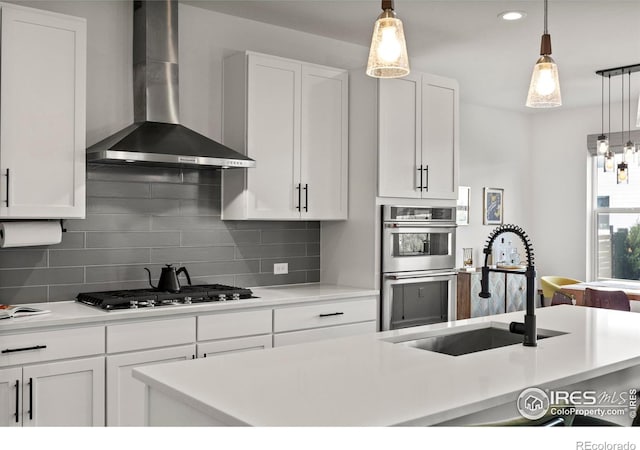 kitchen featuring wall chimney range hood, appliances with stainless steel finishes, a sink, backsplash, and pendant lighting