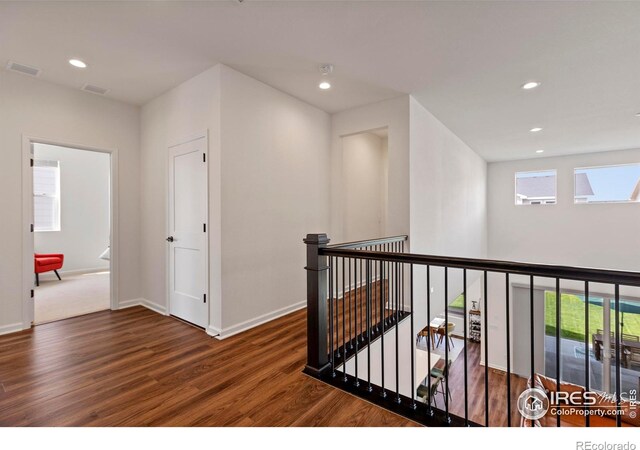 hall with an upstairs landing, wood finished floors, plenty of natural light, baseboards, and recessed lighting