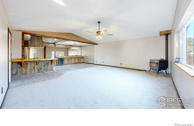 unfurnished living room featuring a wood stove, light carpet, ceiling fan, baseboards, and lofted ceiling