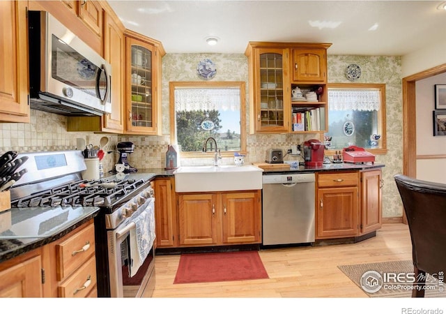 2219 Meadow Green Cir, Franktown, CO 80116 - kitchen featuring stainless steel appliances, a sink, light wood-type flooring, decorative backsplash, and glass insert cabinets