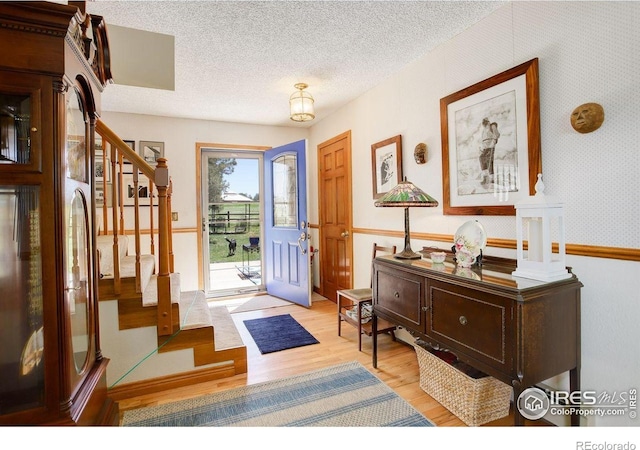 2219 Meadow Green Cir, Franktown, CO 80116 - entrance foyer featuring stairs, light wood-style flooring, a textured ceiling, and wallpapered walls