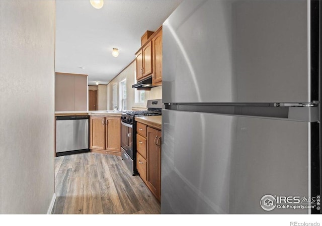 830 1st St # 14, Pierce, CO 80650 - kitchen with stainless steel appliances, brown cabinets, light wood finished floors, and under cabinet range hood