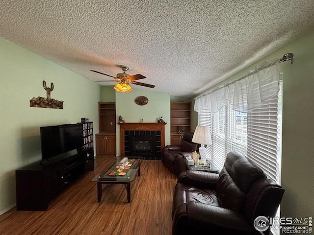 living room with wood finished floors, a ceiling fan, a textured ceiling, and a tile fireplace