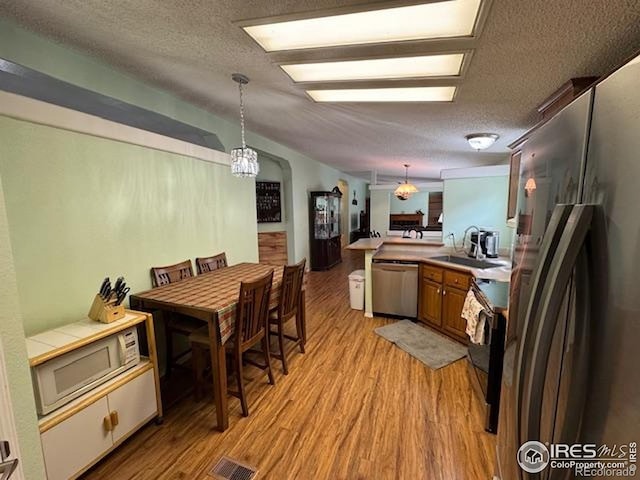 kitchen featuring appliances with stainless steel finishes, light wood-style flooring, a sink, a peninsula, and a textured ceiling