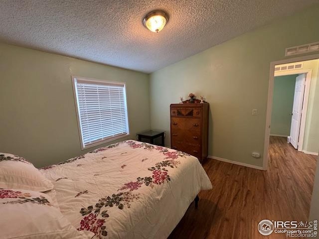 bedroom featuring wood finished floors, a textured ceiling, and baseboards