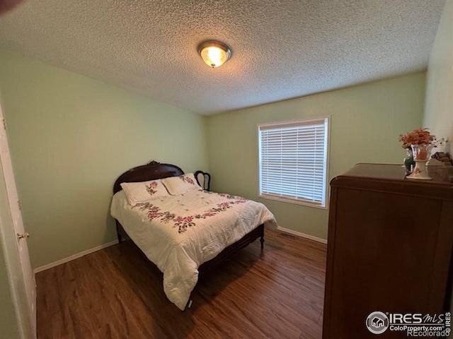 bedroom with wood finished floors, a textured ceiling, and baseboards