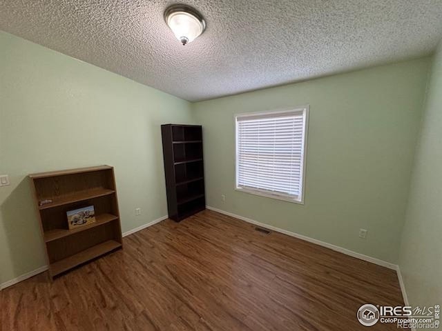 spare room featuring wood finished floors, a textured ceiling, and baseboards