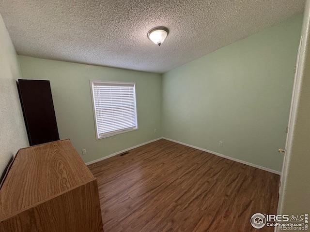empty room with wood finished floors, a textured ceiling, and baseboards