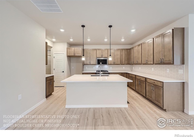 kitchen featuring a sink, stainless steel microwave, light wood-style flooring, backsplash, and recessed lighting